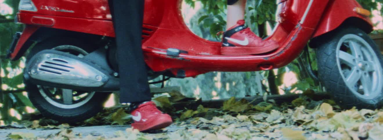 Woman with red sneakers and black pants sits on red motor scooter