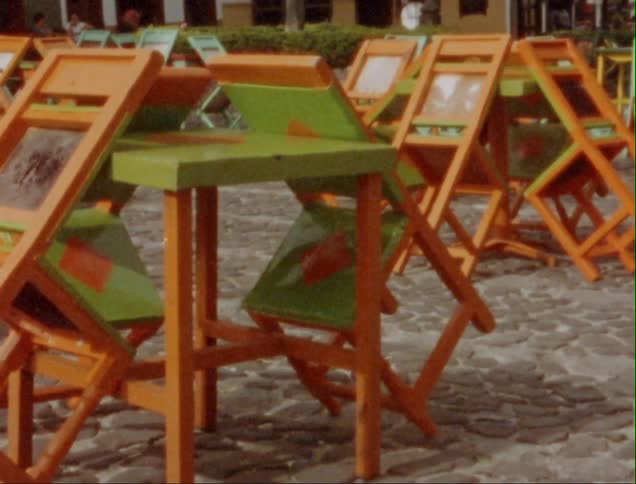 Chairs leaning against tables in a courtyard with people in the background