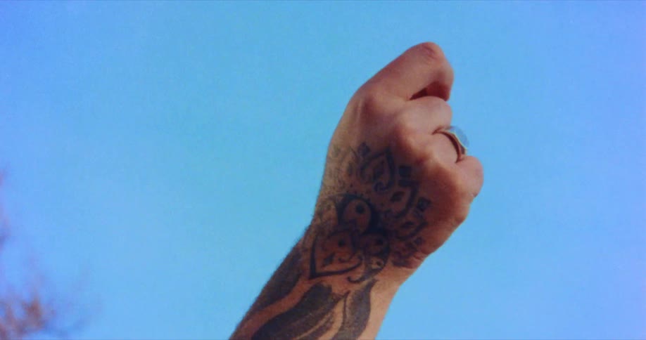 Person with tattooed arm and hand shakes fist in air