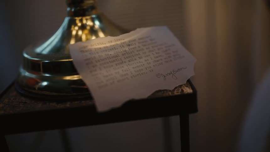 Letter typed on a piece of paper resting over a small table under a lamp inside a dimly lit room