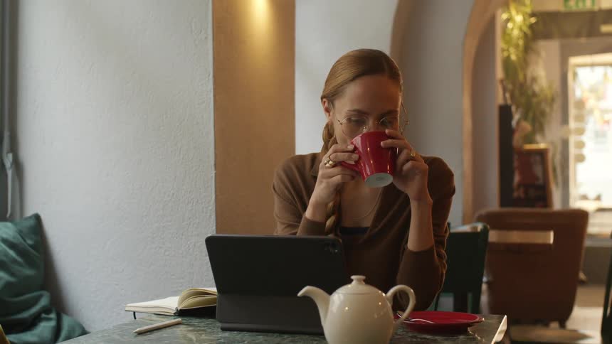 Woman drinking a cup of coffe at a restaurant while looking at a laptop