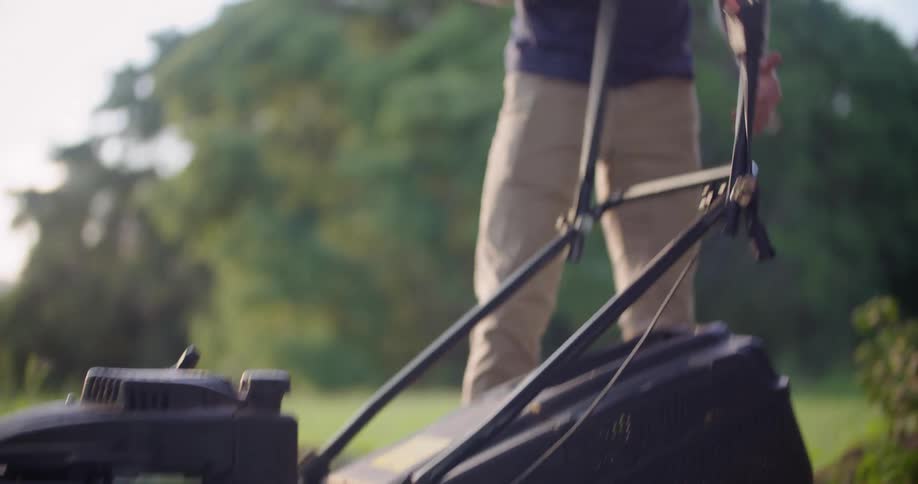 Man assembling a lawnmower starts the motor in a field at morning
