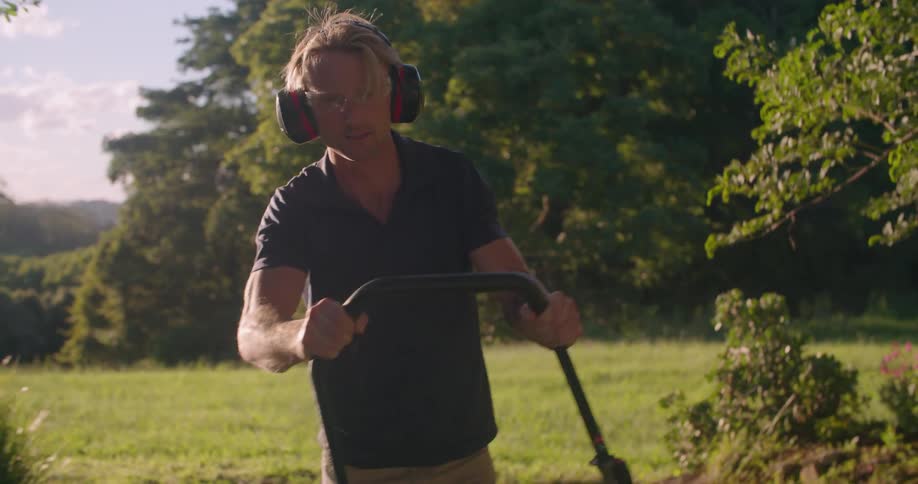 A man pushes a rototiller in a grassy field