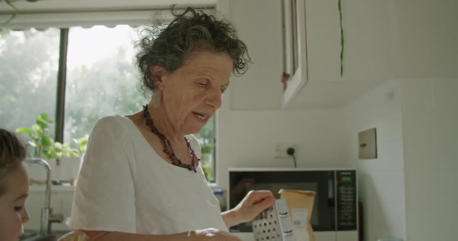 Grandmother cooking in the kitchen at home while granddaughter eats batter from a spoon
