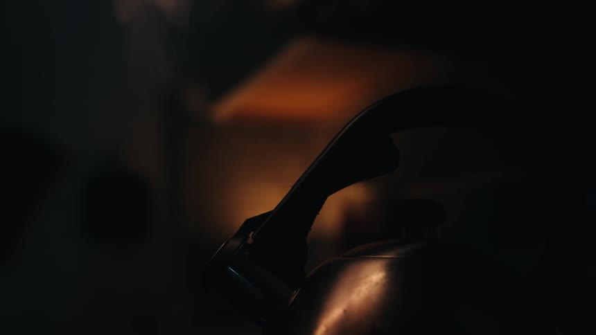 Steam rises from a tea kettle in a dimly lit room