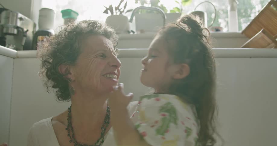 Granddaughter playfully kissing her grandmother in the floor of the kitchen at home