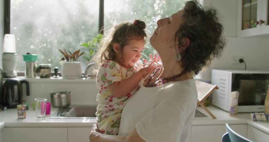 A grandmother holds and talks to her granddaughter in the kitchen