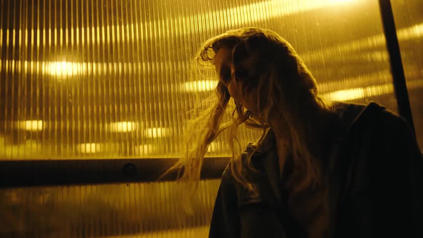Pensive blonde woman with jacket leans against transparent wall at night