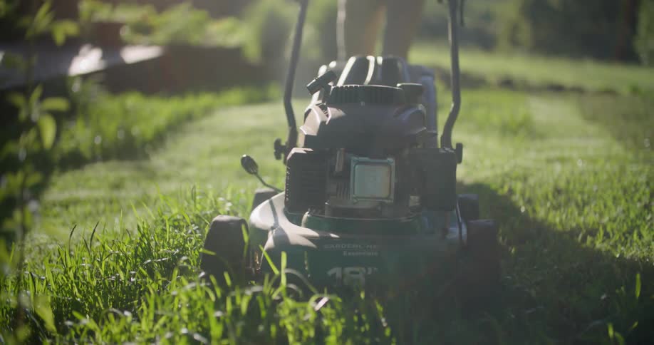 Man wearing earmuffs uses a lawnmower on the backyard in the morning