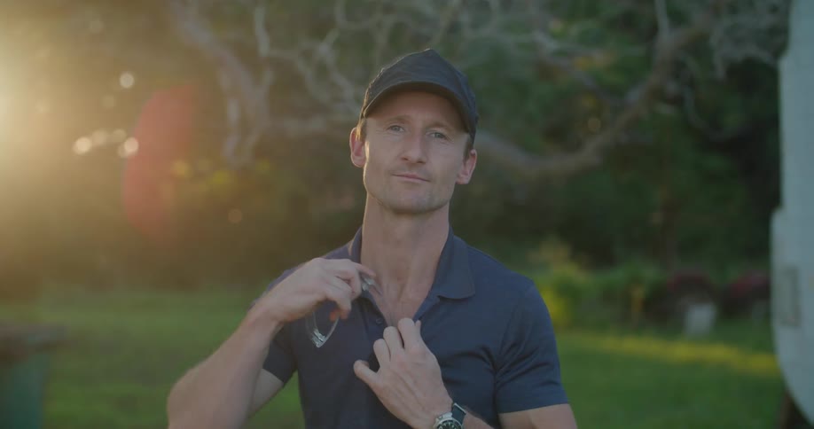 A man takes off clear glasses as he poses outdoors