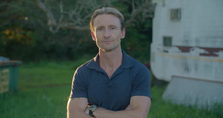 Blonde muscular man wearing blue shirt standing in the grass outdoors at morning
