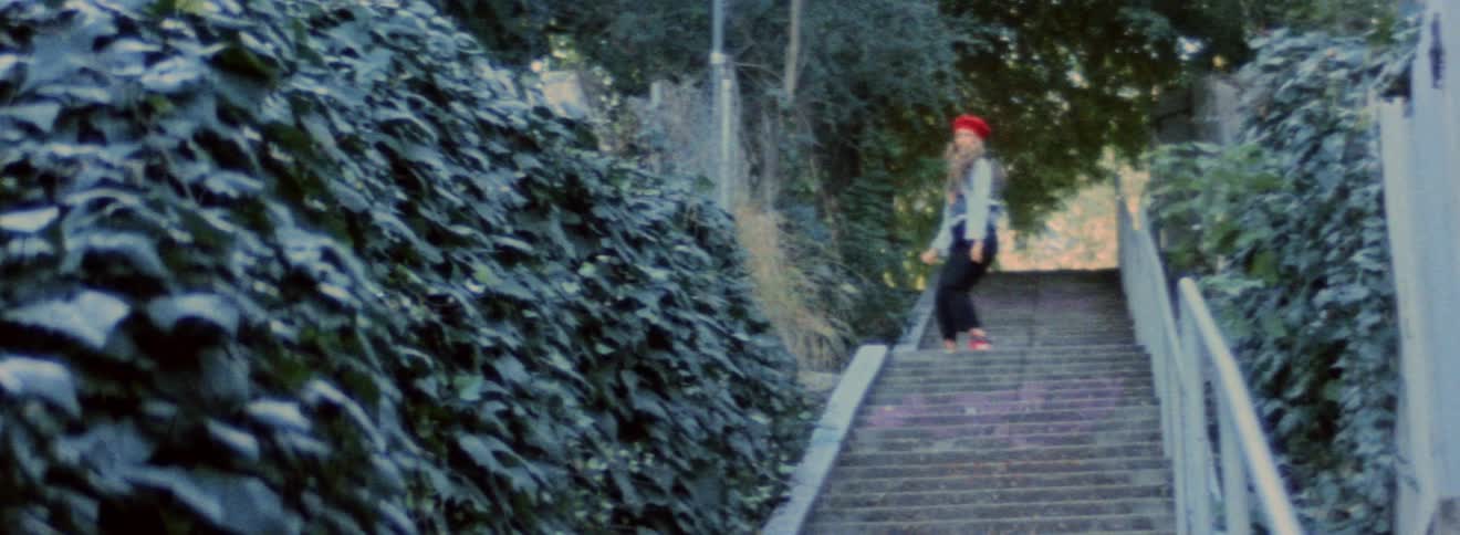 Blonde woman wearing denim jacket and red hat dancing on the stairs outdoor at morning