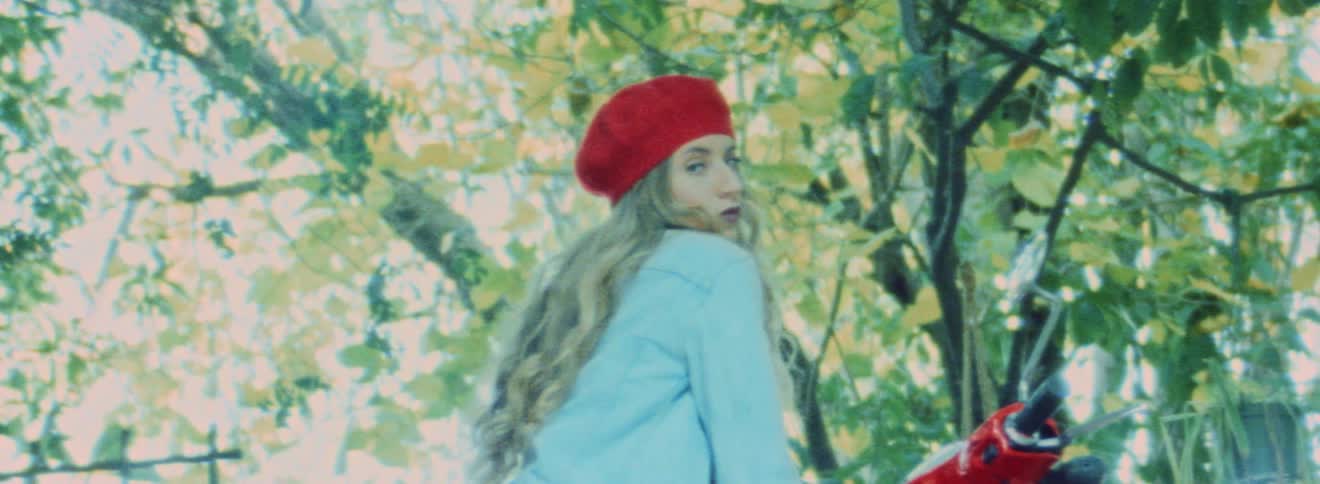 Blonde woman wearing denim jacket and red hat modeling for the camera in front of trees