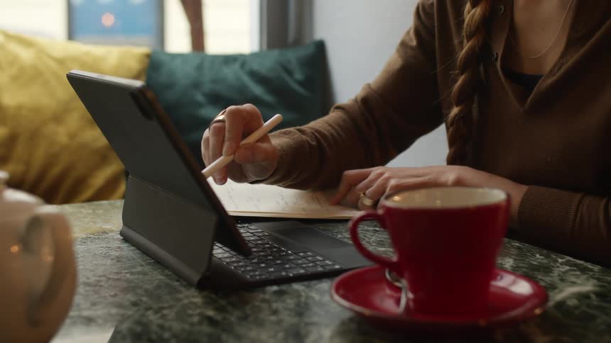 A woman sits at a table using a pen on a tablet computer