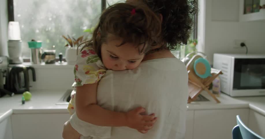 A woman is standing in a kitchen holding a little girl and swaying with her