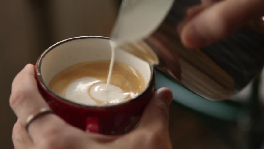 A person pours cream in a latte to make a design