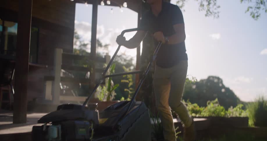 A man pushes a lawn mower outside and wears headphones