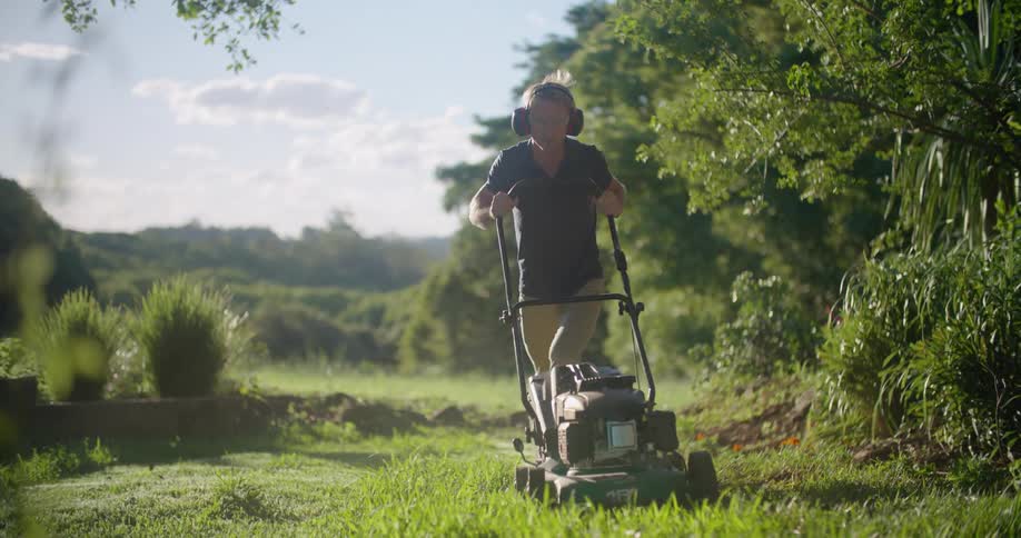 A man is mowing his lawn on a sunny day