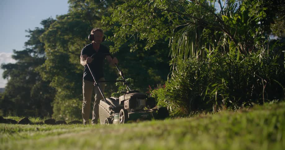 Man wearing hearing protection mowing the lawn on the backyard in the morning