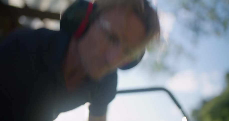 Blonde man with black shirt goggles and headphones starts mower in the countryside