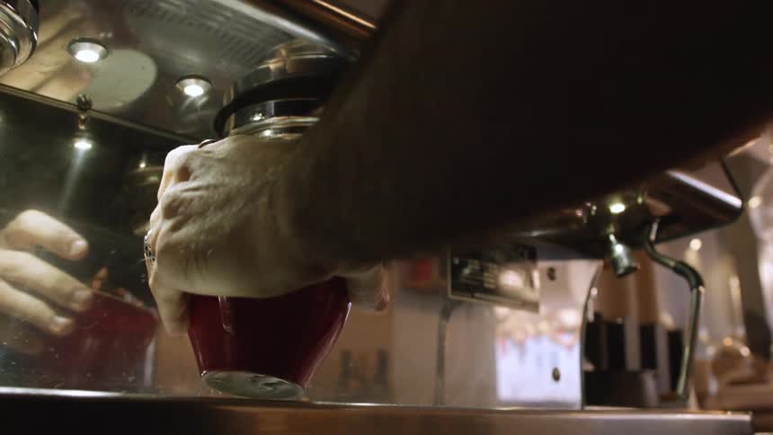 Barista places a filter on an espresso machine and starts pouring hot coffee over a red cup