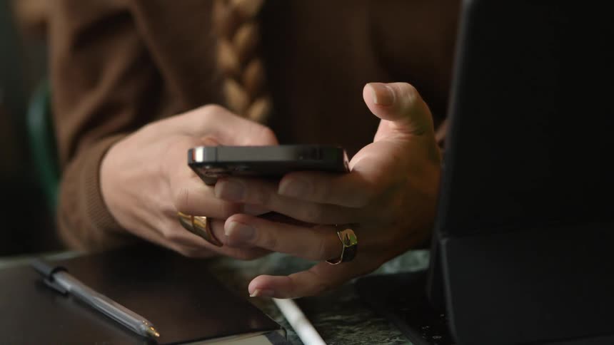 Woman sits at desk in front of computer scrolling on her smartphone