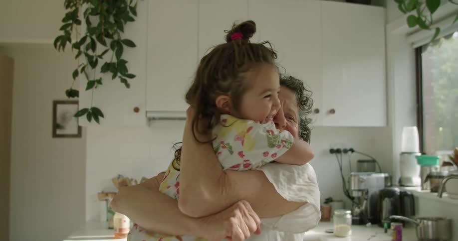 A young girl is in the kitchen with her grandmother and they are happily hugging each other