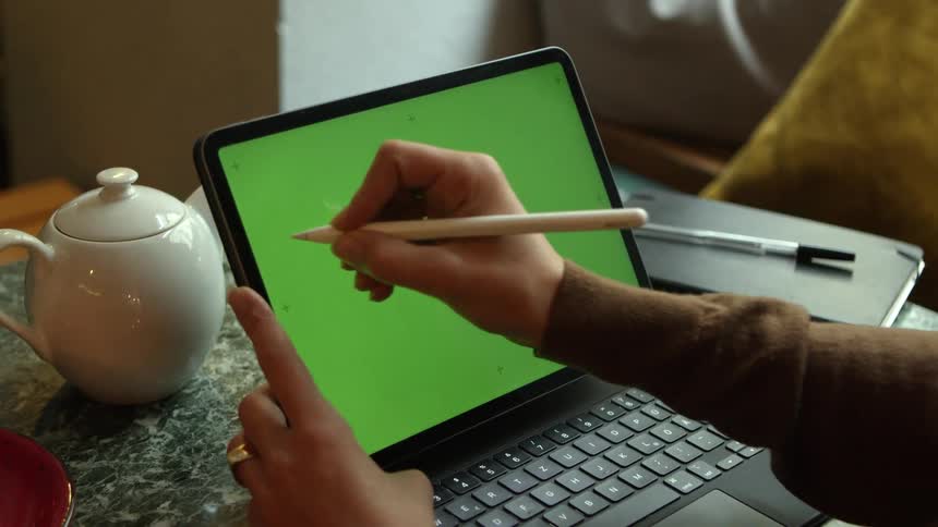 Man with brown sweater uses stylus pen on tablet with keyboard