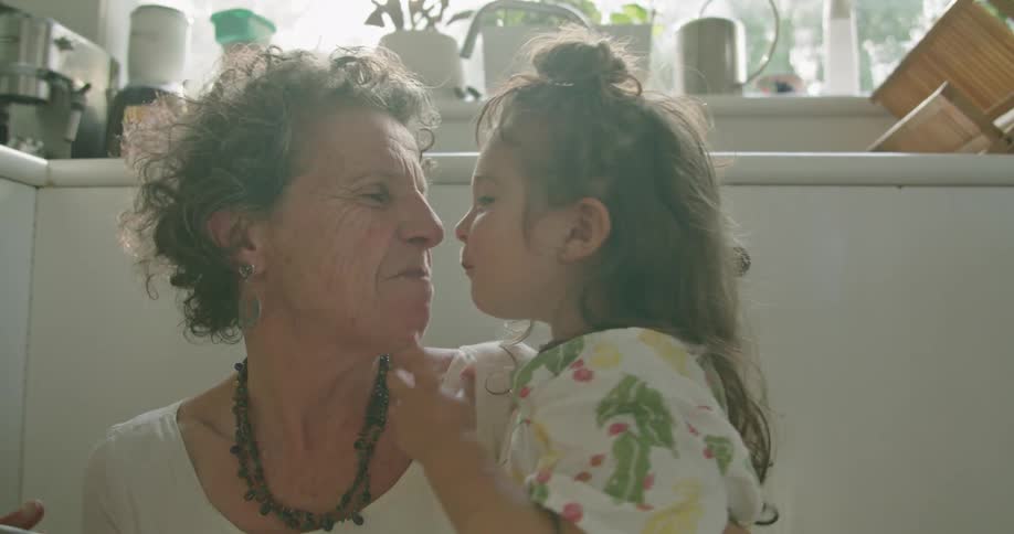 Grandmother hugs granddaughter while working in kitchen then they exchange a kiss