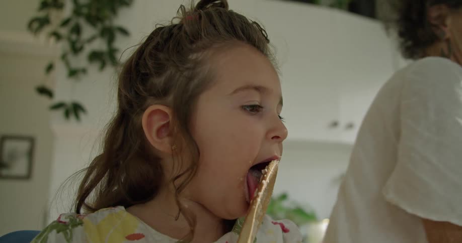 Girl licking a spoon in the kitchen while her grandmother cooks