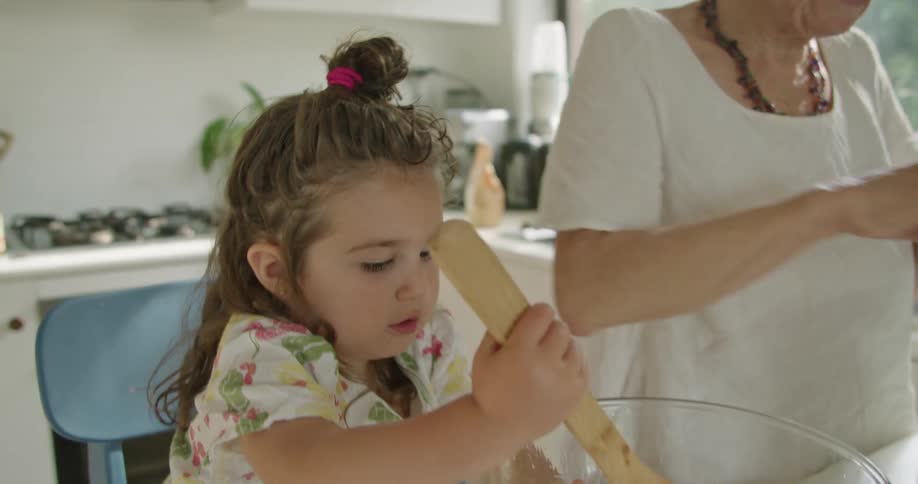 A little girl is preparing food with her grandmother in a kitchen