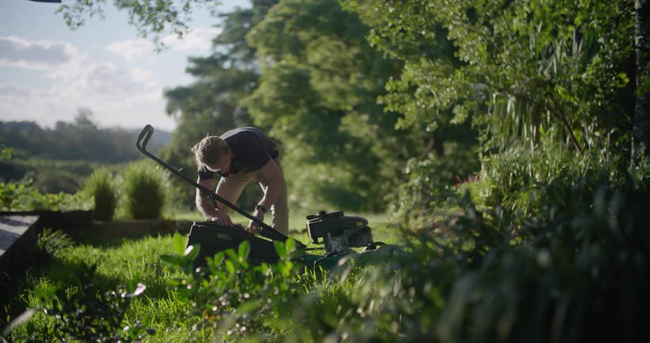 A man is outside attaching a grass catcher to a lawn mower