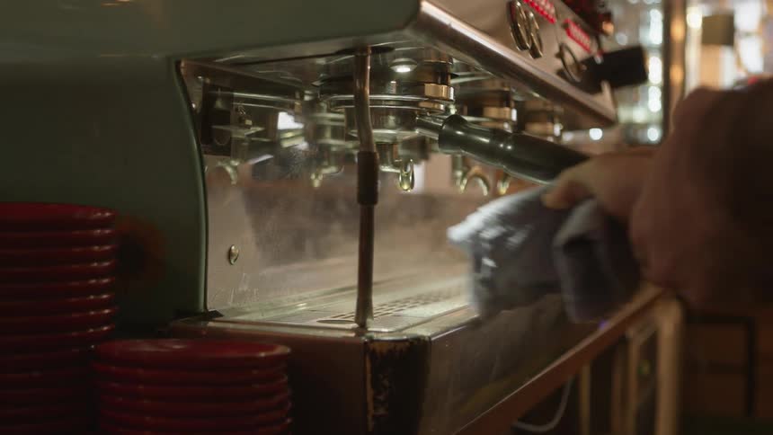 A man wipes down an espresso machine in a coffee shop after steam cleaning it
