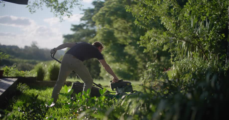 A man is outside starting a lawn mower and cutting the grass