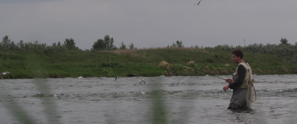 A man fishing while standing in the middle of a lake
