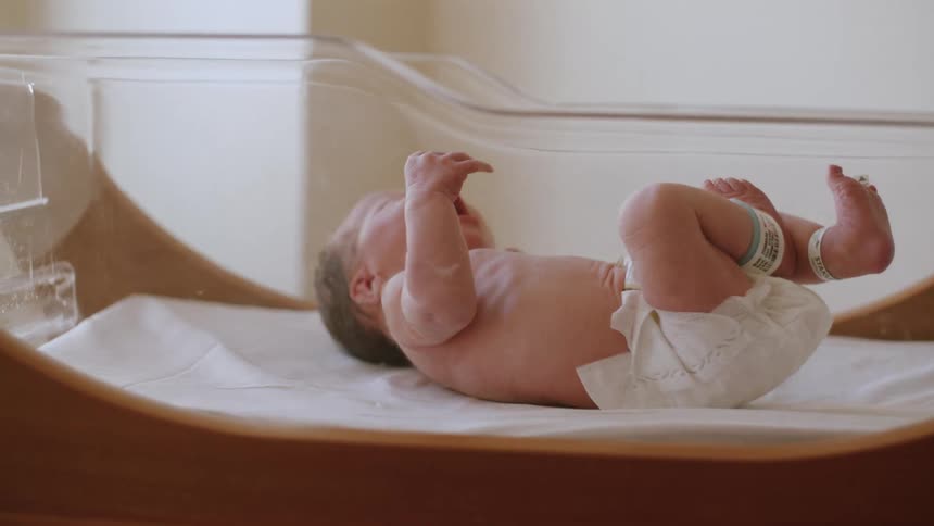A newborn baby is yawning in a crib in hospital