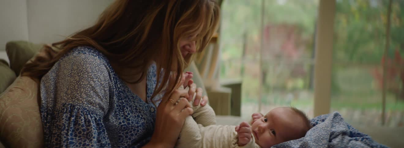 Mother smiles and kisses babies feet while she sits on couch with baby in her lap