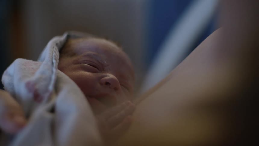 Newborn baby wrapped inside a blanket resting over a mothers chest after birth