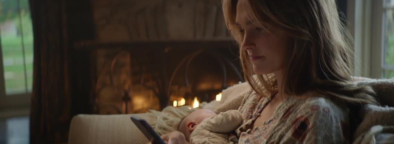A woman looks at her smartphone while holding her sleeping baby