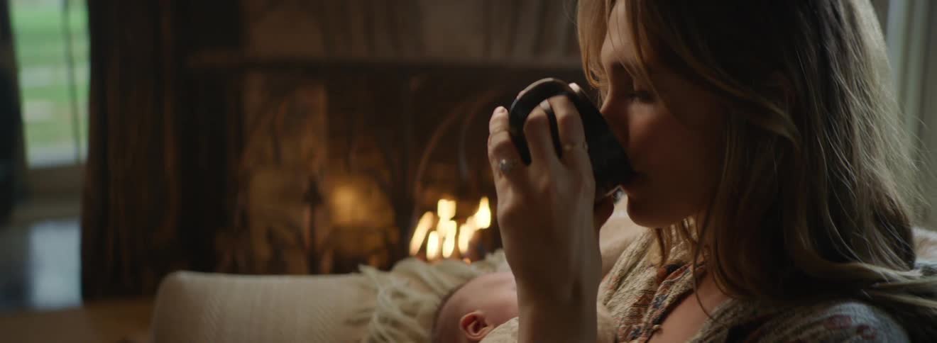 Mother holding a newborn baby in her arms sitting on a couch in front of a fireplace