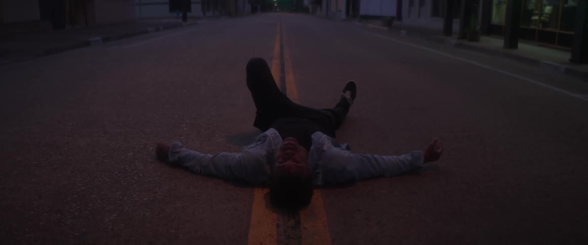 A man is laying in the middle of a street in a small town at night