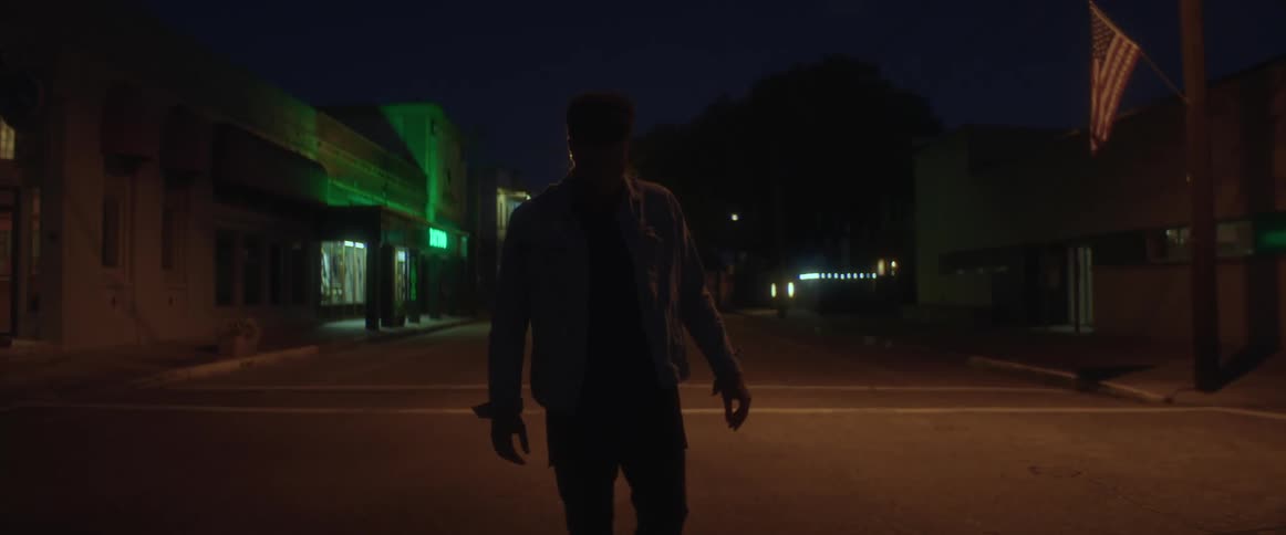 A man is walking in the middle of a road at night in a small town