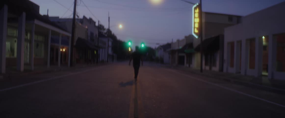 A man is walking down the middle of a street in a small town