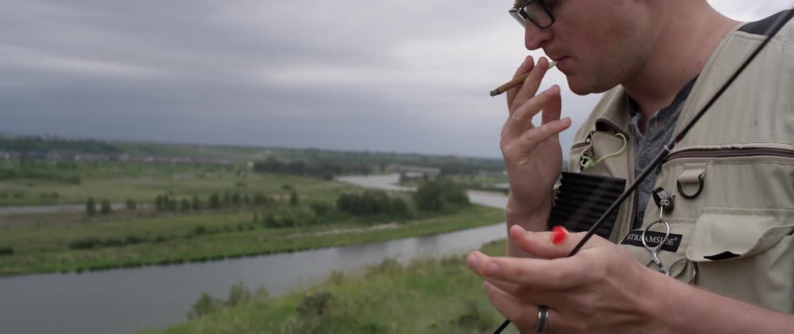 A man smokes a cigar while holding a fishing pole