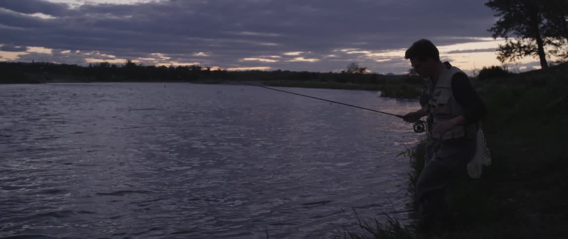 Man fishing on the edge of a lake after sunset