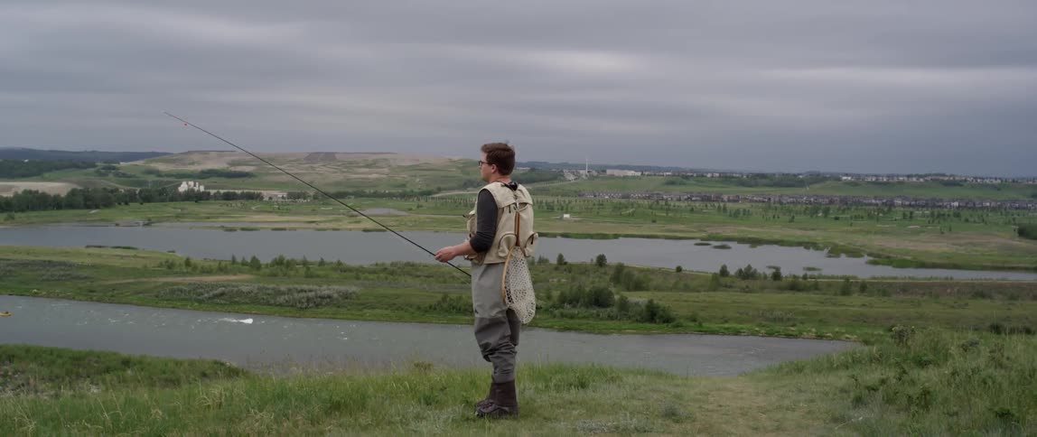 Man with fishing pole standing on a hill overlooking lake