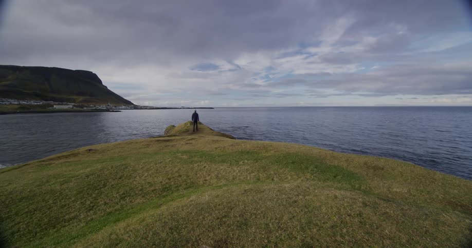 A person walks towards the edge of a cliff near the water