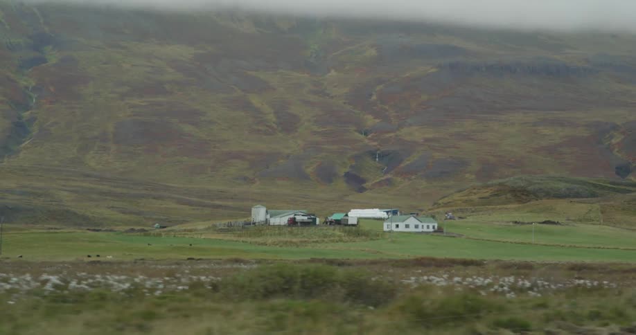 Moving past a farm with a large hill in the distance