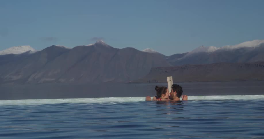 A man and women kiss while in a pool overlooking a mountain range