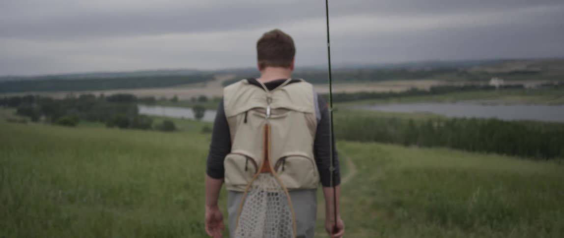 A man is carrying a fishing pole as he walks towards the water